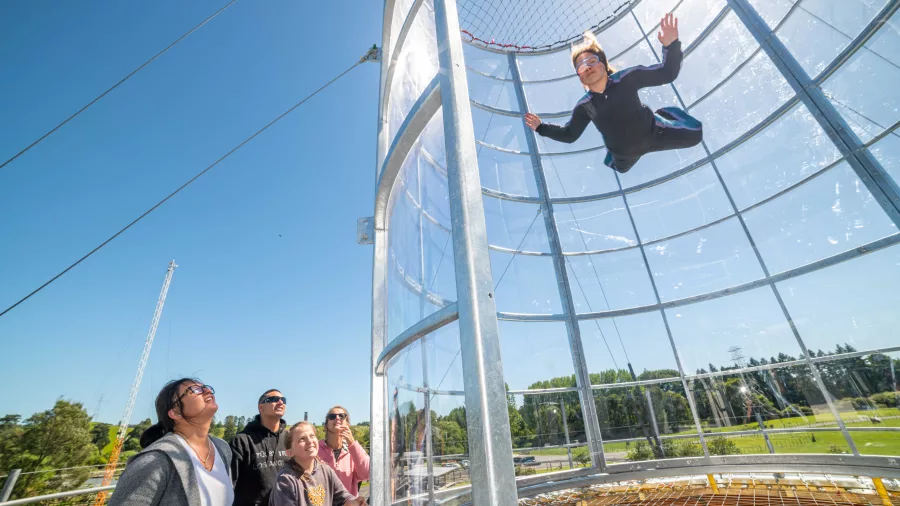 Visitor flying in a vertical wind tunnel at Freefall Xtreme while friends watch from below