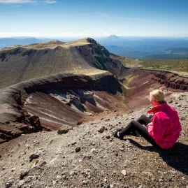 Woman in pink jacket sitting at the crater rim overlooking Mount Tarawera’s volcanic landscape