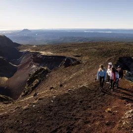Group walking along the rim of Mount Tarawera crater under a clear morning sky