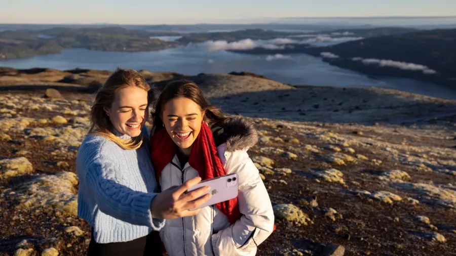 Two women taking a selfie with Lake Tarawera and distant ridges behind them