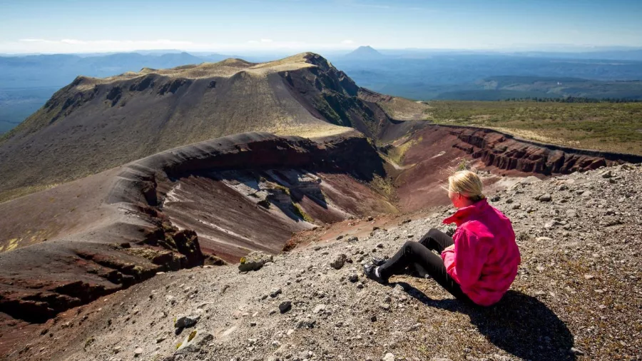 Woman in pink jacket sitting at the crater rim overlooking Mount Tarawera’s volcanic landscape