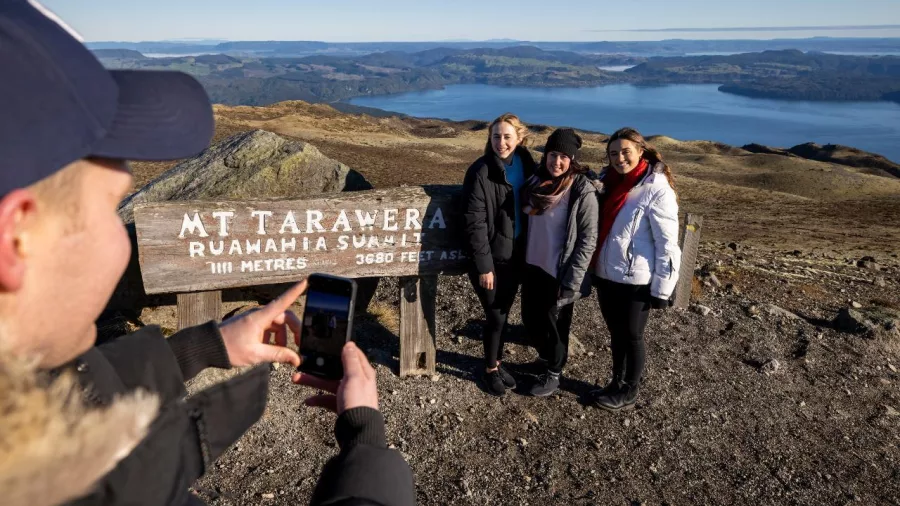 Visitors posing next to the Mount Tarawera summit sign at Ruawāhia Dome