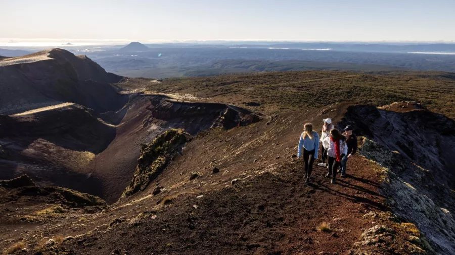 Group walking along the rim of Mount Tarawera crater under a clear morning sky
