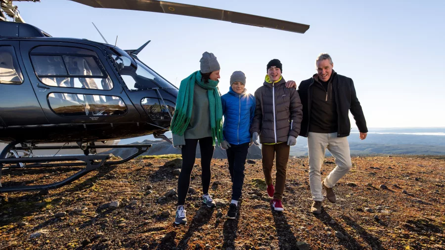 Smiling family with guide walking away from a landed helicopter on Mount Tarawera