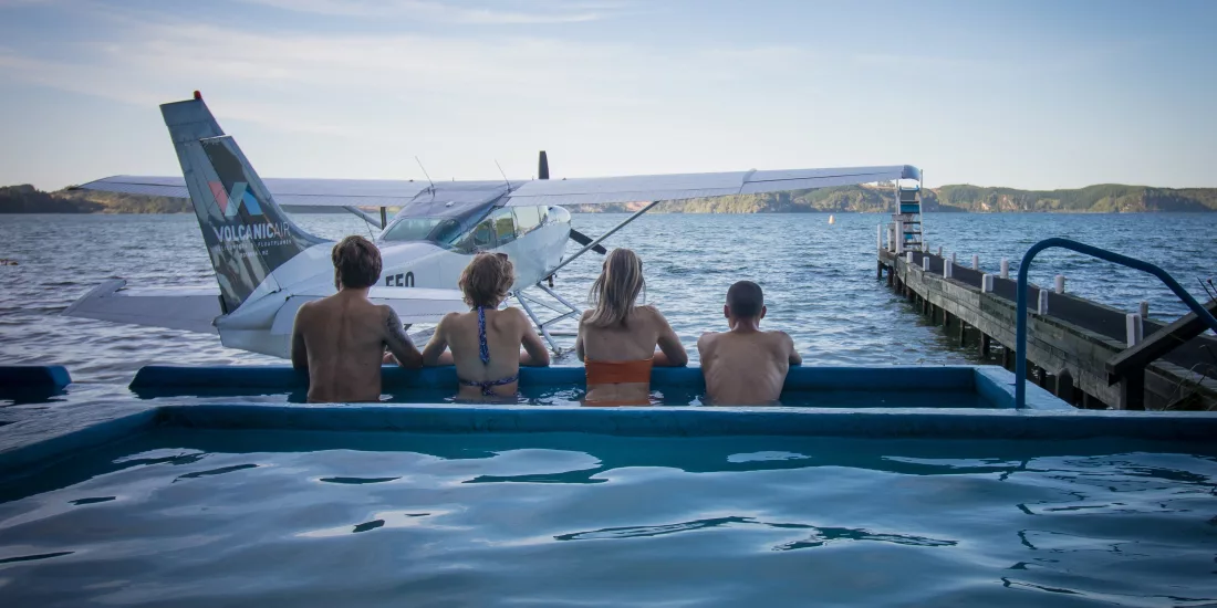 Group of people enjoying a hot pool beside a floatplane at Lake Rotoiti Hot Pools