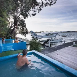Volcanic Air floatplane parked near the jetty at Rotoiti Hot Pools, with people soaking nearby