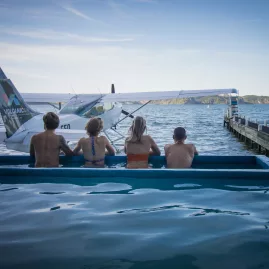 Group of people enjoying a hot pool beside a floatplane at Lake Rotoiti Hot Pools