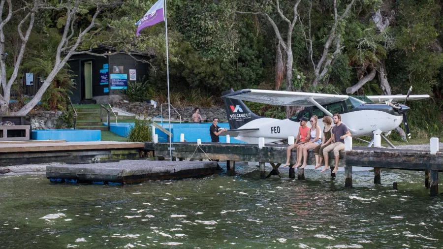 Group sitting on a wooden jetty beside a Volcanic Air floatplane at Lake Rotoiti Hot Pools