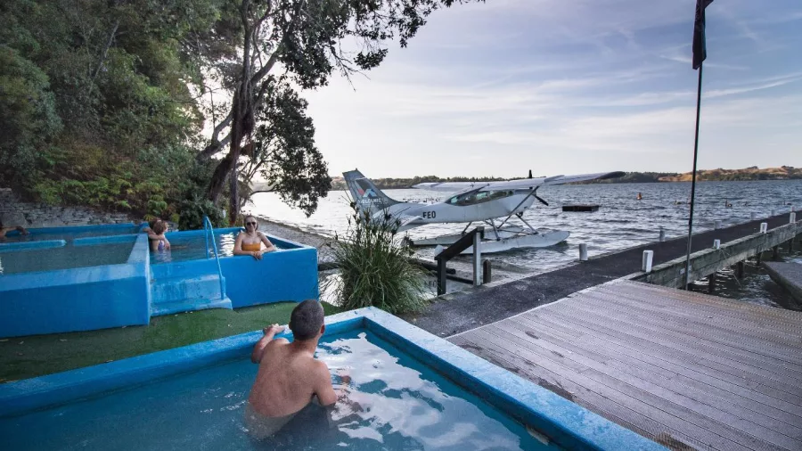 Volcanic Air floatplane parked near the jetty at Rotoiti Hot Pools, with people soaking nearby