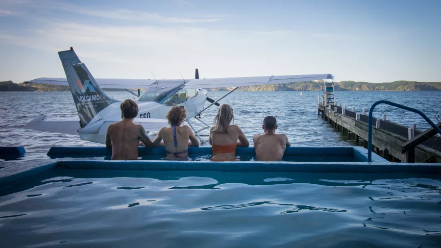 Group of people enjoying a hot pool beside a floatplane at Lake Rotoiti Hot Pools
