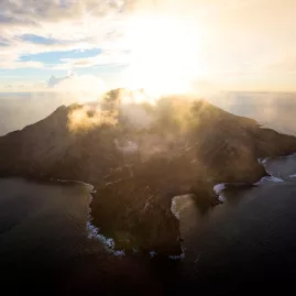 Sun setting behind the volcanic peak of White Island, viewed from the air