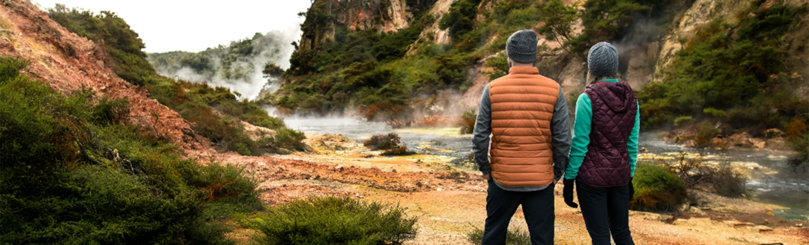 Couple exploring a steaming geothermal valley along a hiking trail in Waimangu Volcanic Valley