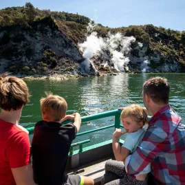 Family watching steam rise from geothermal cliffs during a Lake Rotomahana cruise in Waimangu