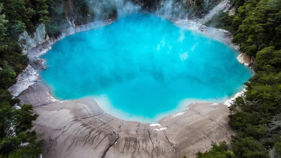 Brilliant blue Inferno Crater steaming in the middle of native forest in Waimangu Volcanic Valley