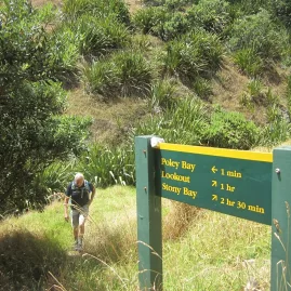 Hiker approaching a DOC track sign pointing to Poley Bay and Stony Bay on the Coromandel Coastal