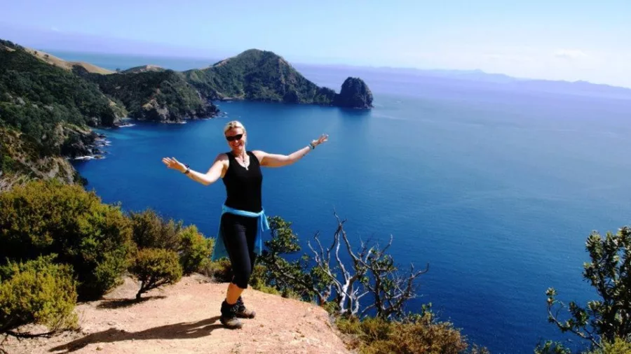 Woman hiker posing at a lookout on the Coromandel Coastal Walkway with cliffs and Pacific Ocean views