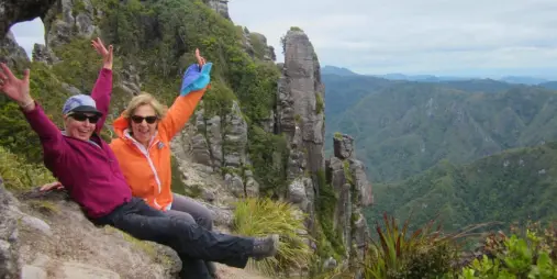 Two hikers celebrating near a dramatic rock formation along the Pinnacles Track in the Coromandel Ranges