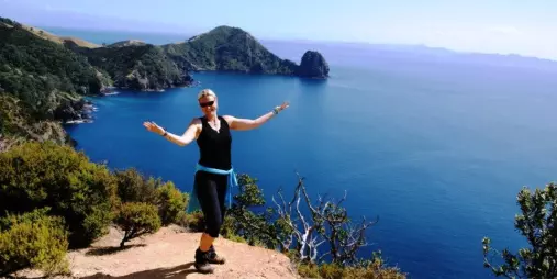 Woman hiker posing at a lookout on the Coromandel Coastal Walkway with cliffs and Pacific Ocean views