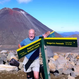Man standing beside signpost at Tongariro Summit on the Alpine Crossing