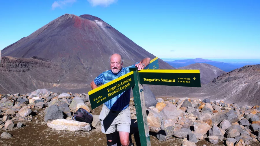Man standing beside signpost at Tongariro Summit on the Alpine Crossing