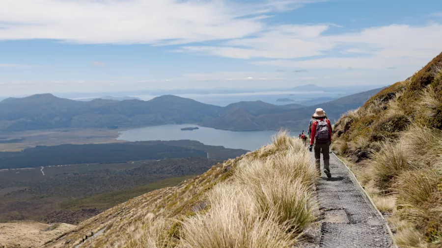 Hiker descending the Tongariro Alpine Crossing with Lake Rotoaira below and Lake Taupō in the far distance