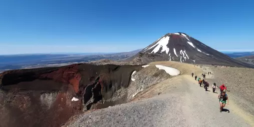 Hikers walking along crater ridge trail with snow-capped Mount Ngauruhoe in the distance