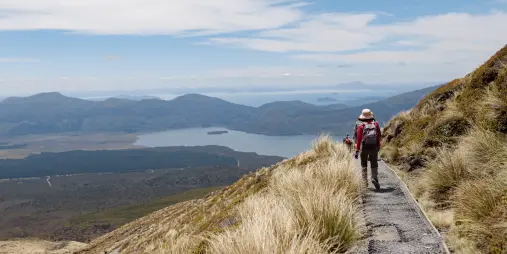 Hiker descending the Tongariro Alpine Crossing with Lake Rotoaira below and Lake Taupō in the far distance