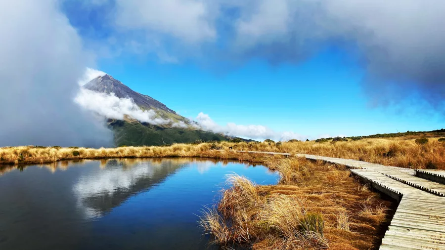 Mt Taranaki reflected perfectly in the calm Pouakai Tarns with a boardwalk in the foreground