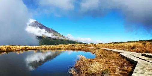 Mt Taranaki reflected perfectly in the calm Pouakai Tarns with a boardwalk in the foreground