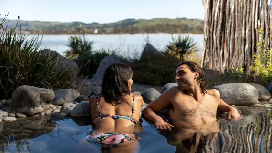 Couple relaxing in a hot mineral pool with lake views at Polynesian Spa, Rotorua, New Zealand