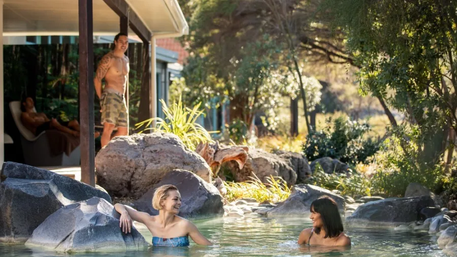 Visitors relaxing in an outdoor rock pool at Polynesian Deluxe Lake Spa, Rotorua, New Zealand