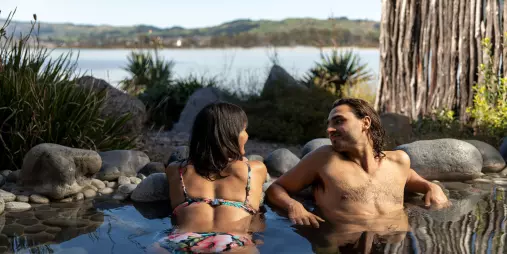 Couple relaxing in a hot mineral pool with lake views at Polynesian Spa, Rotorua, New Zealand