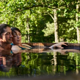 Couple relaxing in a cedar hot tub surrounded by lush greenery at Secret Spot Hot Tubs, Rotorua, New Zealand