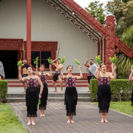 Māori performers in traditional dress performing a haka pōhiri in front of a wharenui at Te Puia in Rotorua