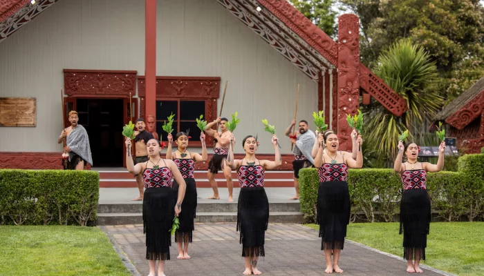 Māori performers in traditional dress performing a haka pōhiri in front of a wharenui at Te Puia in Rotorua
