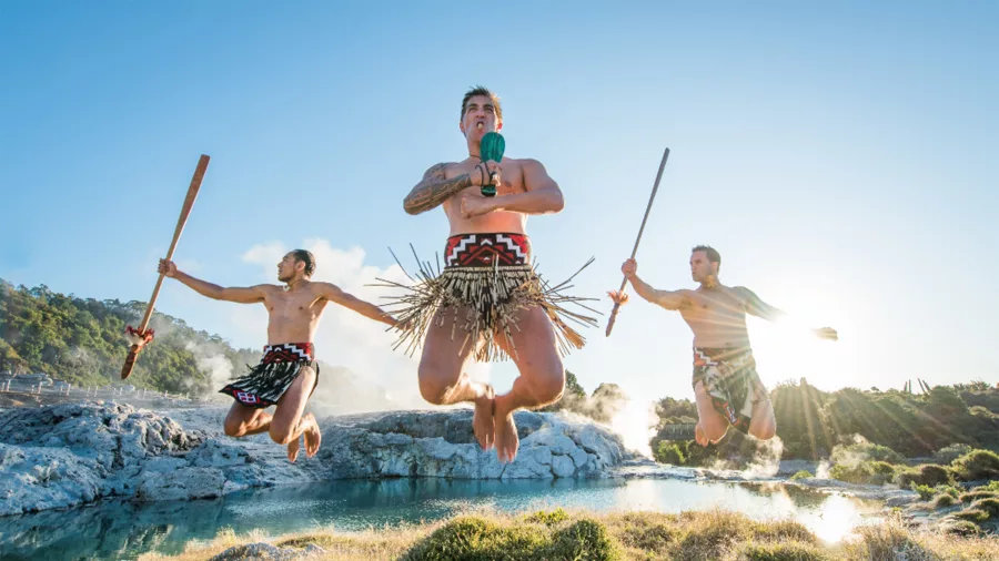 Three Māori performers mid-air with traditional weapons during a cultural show at Te Puia in Rotorua