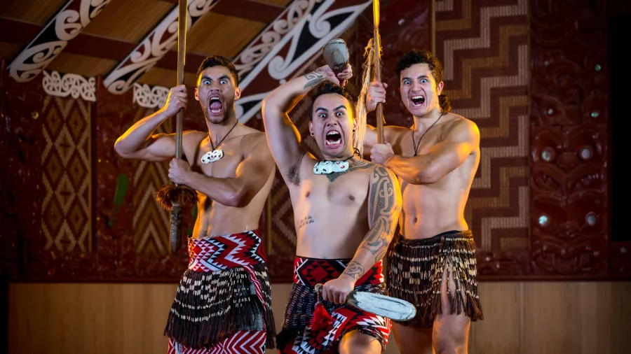 Three Māori warriors performing traditional haka inside wharenui at Te Puia, Rotorua