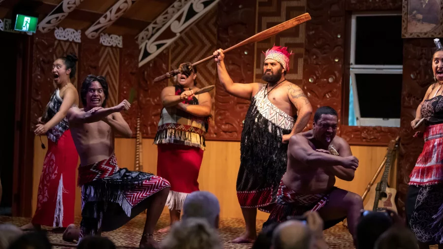 Māori performers striking powerful poses on stage during a haka performance inside a carved wharenui