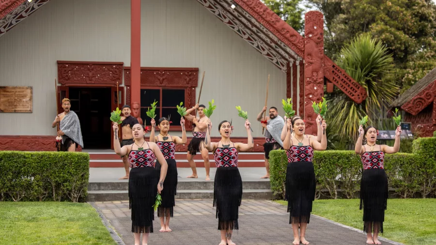 Māori performers in traditional dress performing a haka pōhiri in front of a wharenui at Te Puia in Rotorua