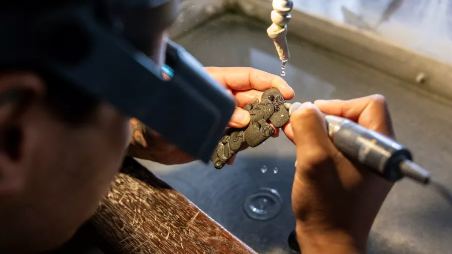 Artist carving intricate greywacke stone design at Te Puia, Rotorua