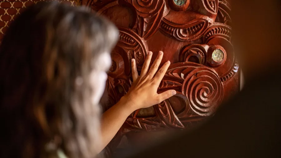 Visitor touching an intricate traditional Māori carving at Te Puia, Rotorua