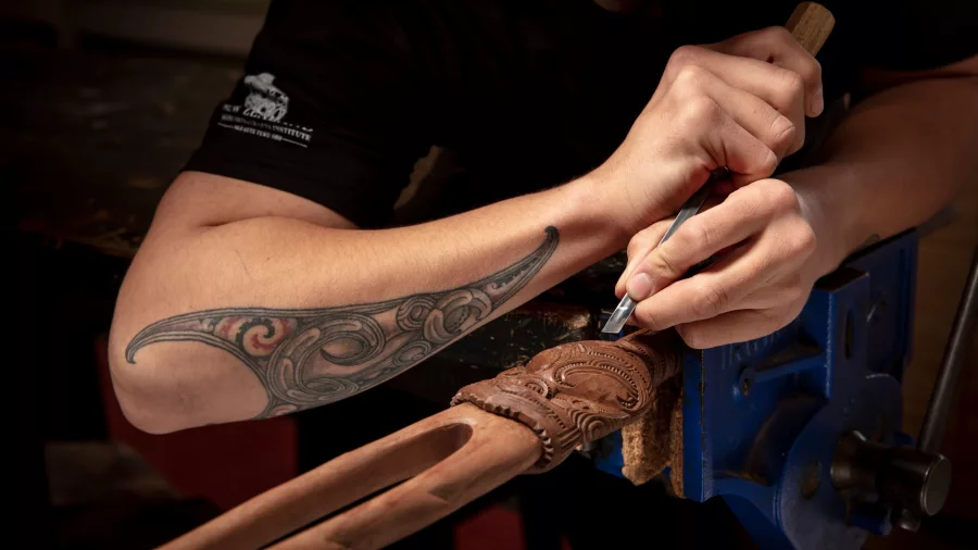 Māori artist carving traditional patterns into wood at Whakairo Rākau in Te Puia, Rotorua