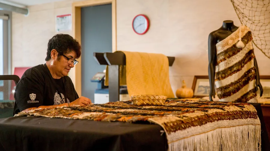 Māori weaver from Te Rito working on a fine feather cloak at Te Puia, Rotorua