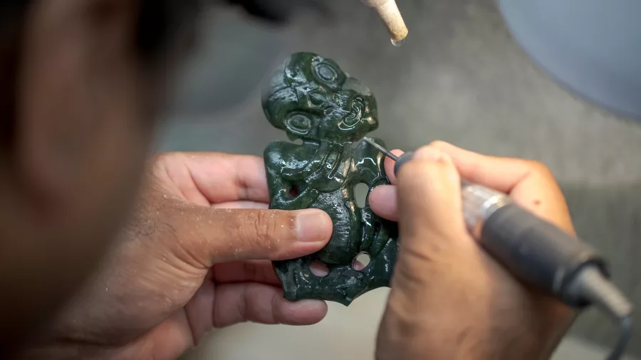 Close-up of a carver’s hands working on a detailed pounamu (greenstone) design at Te Takapū, Te Puia’s carving school in Rotorua