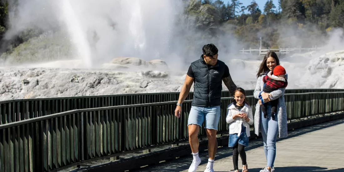 Family walking along a boardwalk with steam rising from geysers in the background at Te Puia in Rotorua