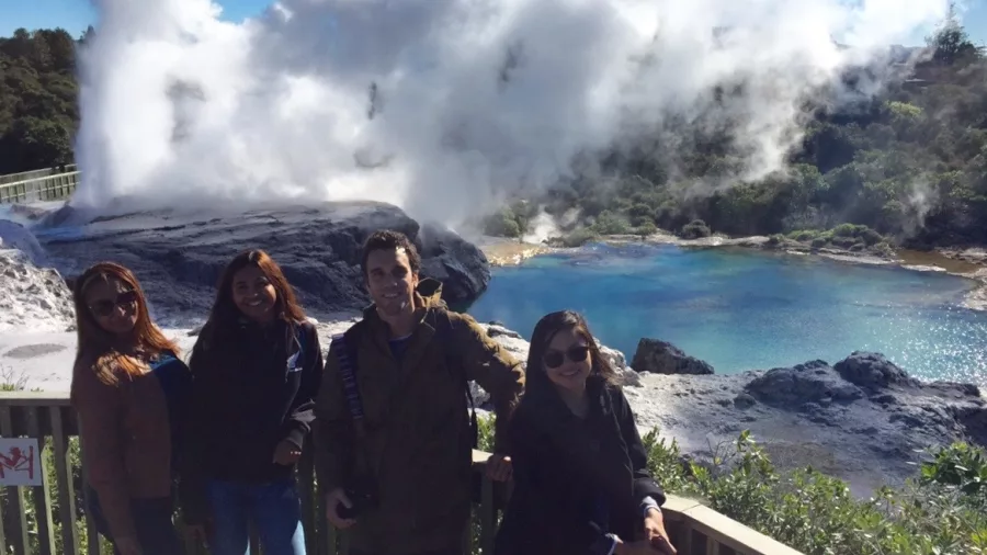 Visitors standing on a platform near Pōhutu Geyser with steam and a blue pool at Te Puia