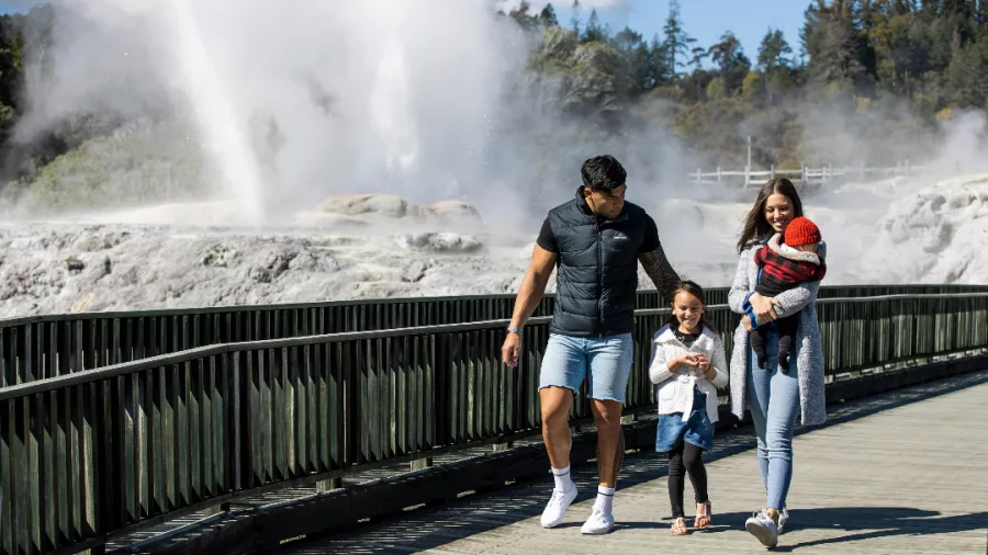 Family walking along a boardwalk with steam rising from geysers in the background at Te Puia in Rotorua