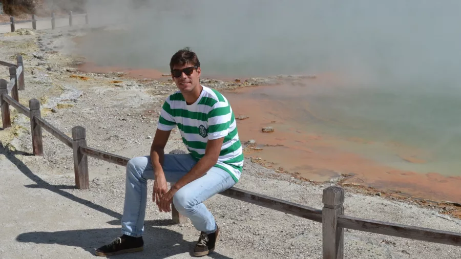 Man sitting on a railing beside the steaming Champagne Pool at Wai-O-Tapu
