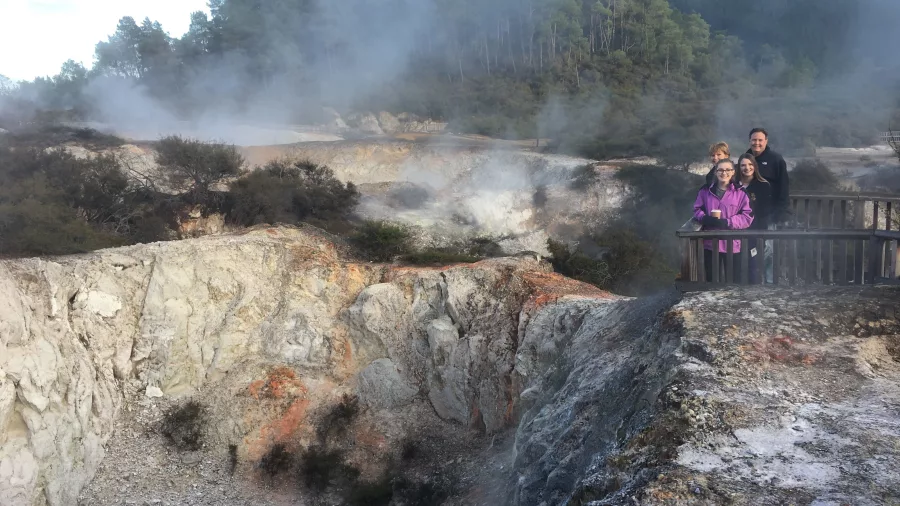 Family viewing The Devil’s Home geothermal crater with rising steam at Wai-O-Tapu, Rotorua