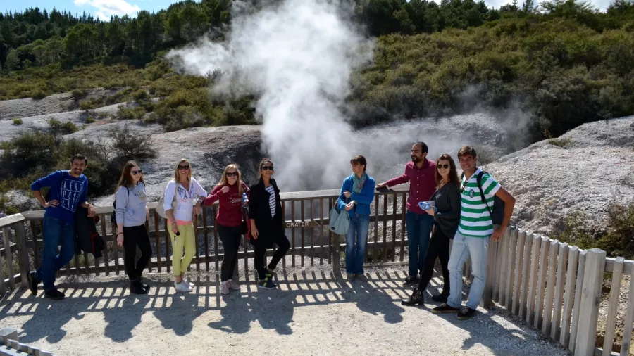Group of tourists standing at Rainbow Crater in Wai-O-Tapu Thermal Wonderland with steam rising from the geothermal landscape